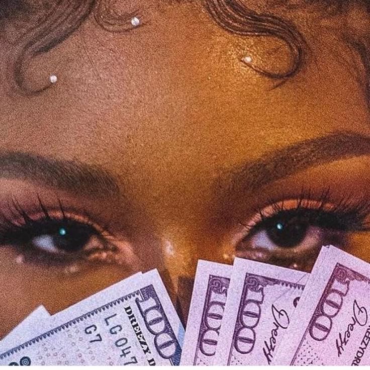 Close-up of a woman's eyes holding a fan of hundred-dollar bills